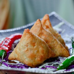 Crispy Indian samosas served with chili peppers and cabbage garnish.